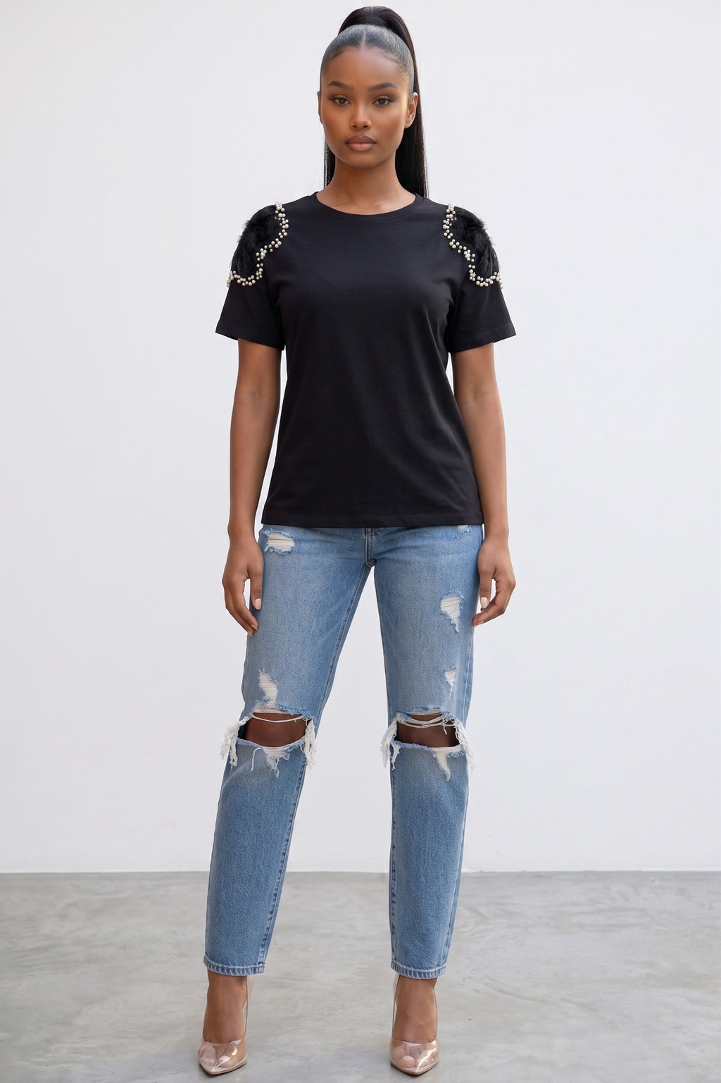 Model wearing Hush Boutique black knit shirt with sheer floral shoulders, pearl and crystal embellishments, and jeans.