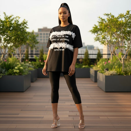 Hush Boutique black oversized t-shirt with white floral trim and graphic text. Model wears leggings and clear heels.