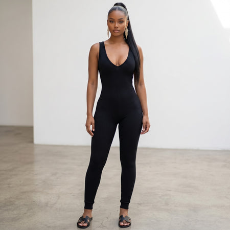 Model wearing a black Hush Boutique ribbed sleeveless jumpsuit with a deep V-neckline in a minimalist studio setting.