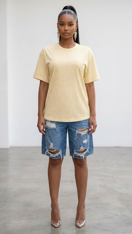 Model wearing a Hush Boutique pale yellow oversized t-shirt with rhinestone studs and distressed denim shorts.